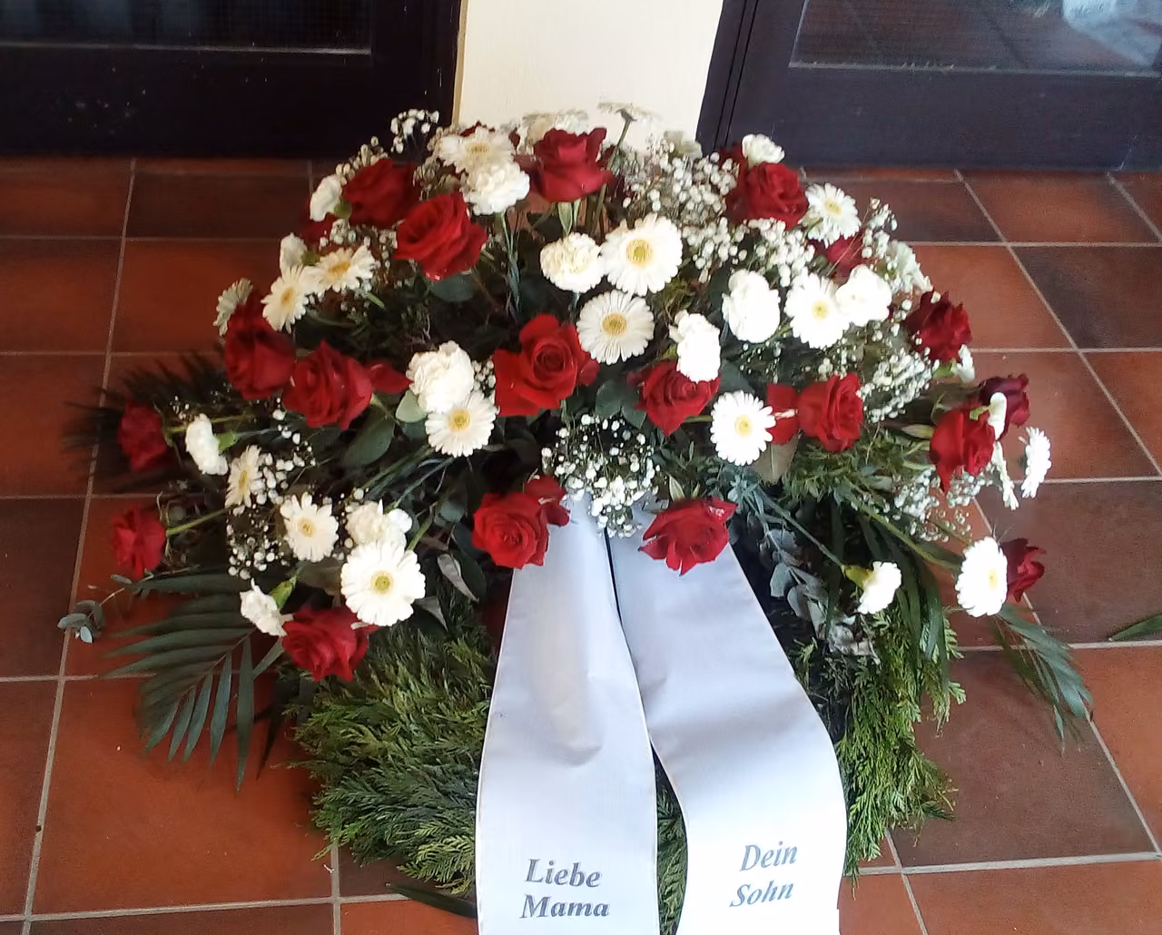 Gesteck aus roten und weißen Rosen mit Schleifen