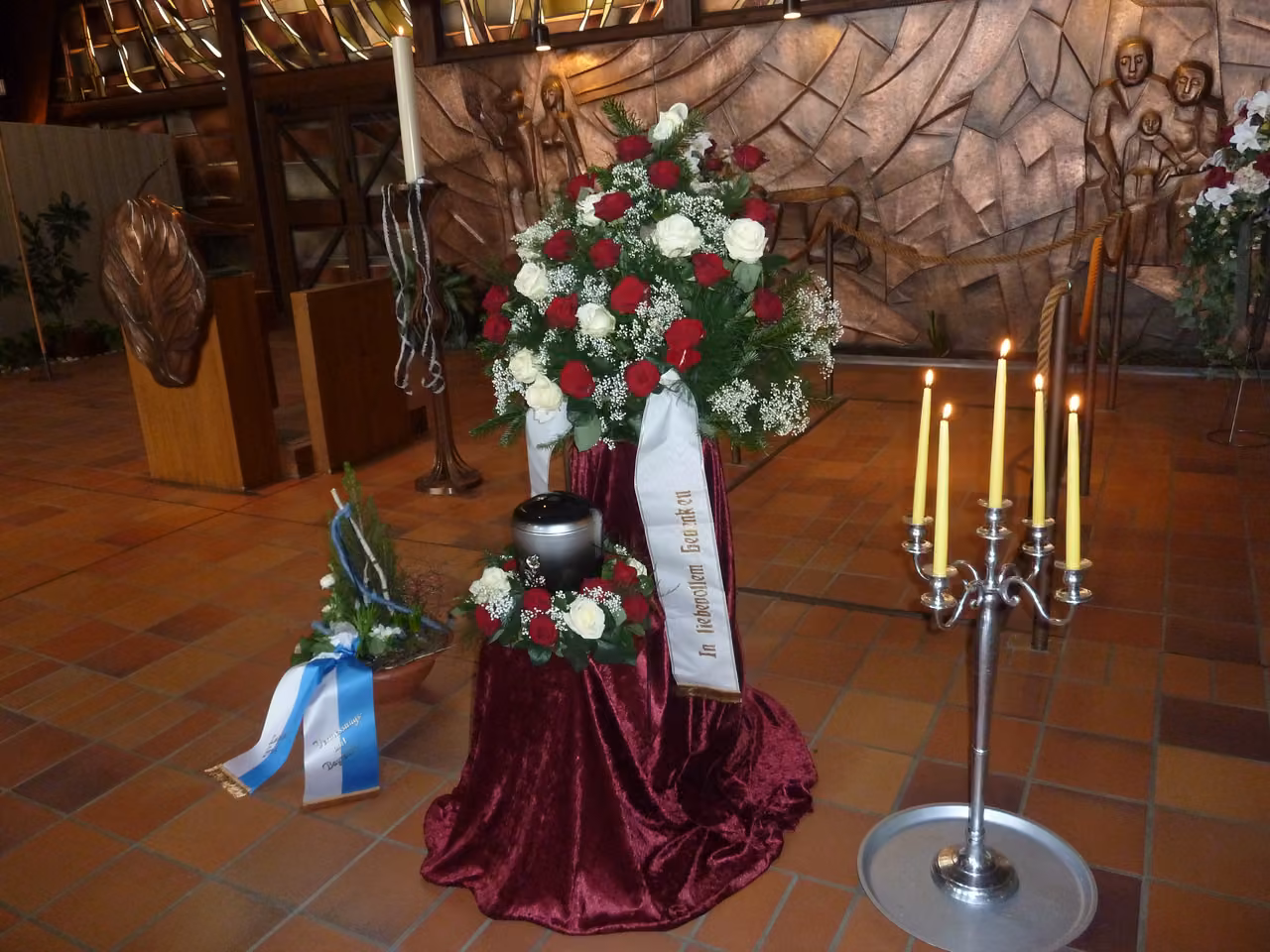 Urne mit Rosenkranz auf rotem Samt neben Kerzenleuchtern